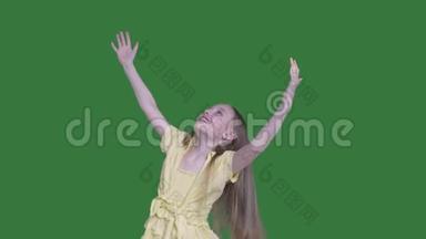 快乐的少女举起双手在绿色的背景上扭动。 微笑的女孩伸出双手享受快乐